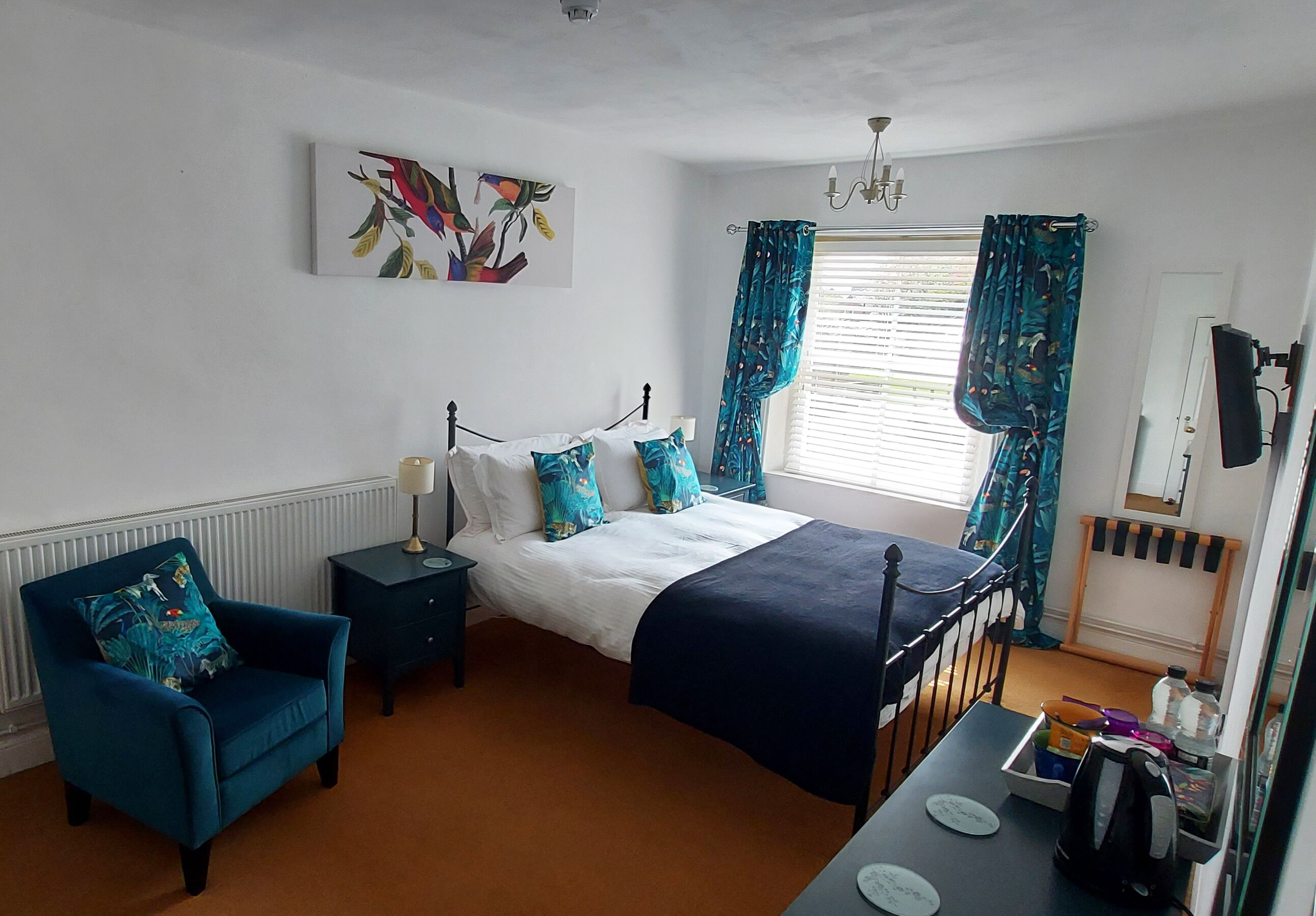 A bedroom with a bed, a chair, a nightstand, a dresser, a window with curtains, and a painting on the wall.