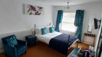 A bedroom with a bed, a chair, a nightstand, a dresser, a window with curtains, and a painting on the wall.