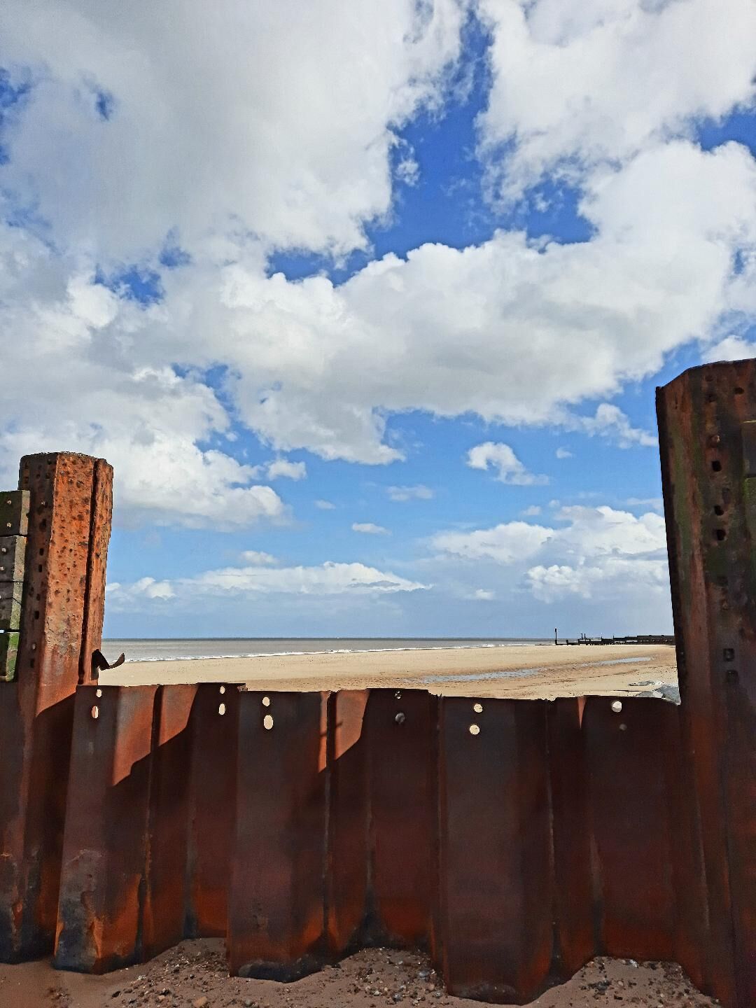 A beach with a rusty metal barrier in the foreground.
