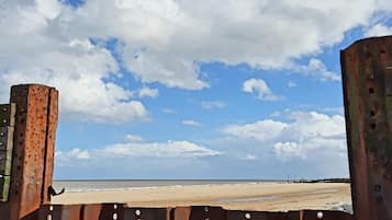 Una playa con una barrera metálica oxidada en primer plano.