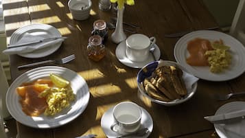 A wooden table with breakfast items including eggs, smoked salmon, toast, and a flower vase.