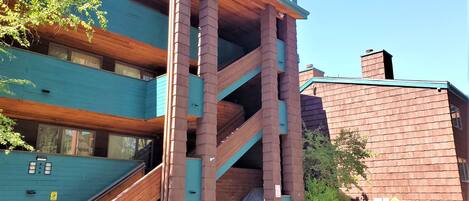 Un edificio de varios pisos con fachada de madera y detalles verdes, que incluye una escalera y un vestíbulo cubierto.