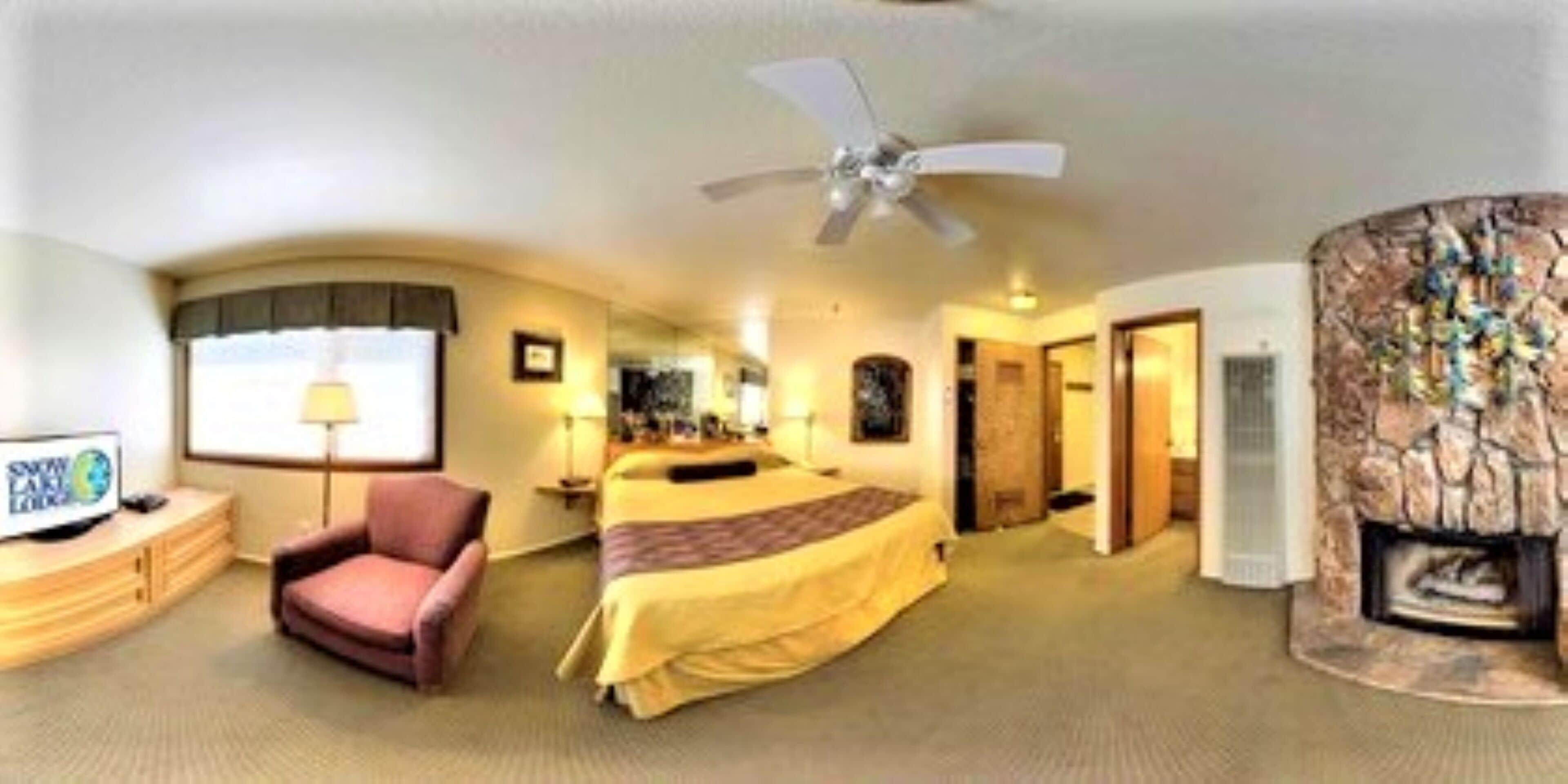 A hotel room with a bed, a chair, a television, a fireplace, and a ceiling fan.