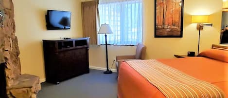 Hotellihuone, jossa on sänky, työpöytä, televisio, kattotuuletin ja taulu seinällä.