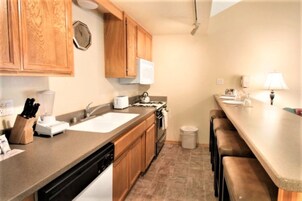 A compact kitchen with wooden cabinets, a sink, a stove, and a bar area with stools.