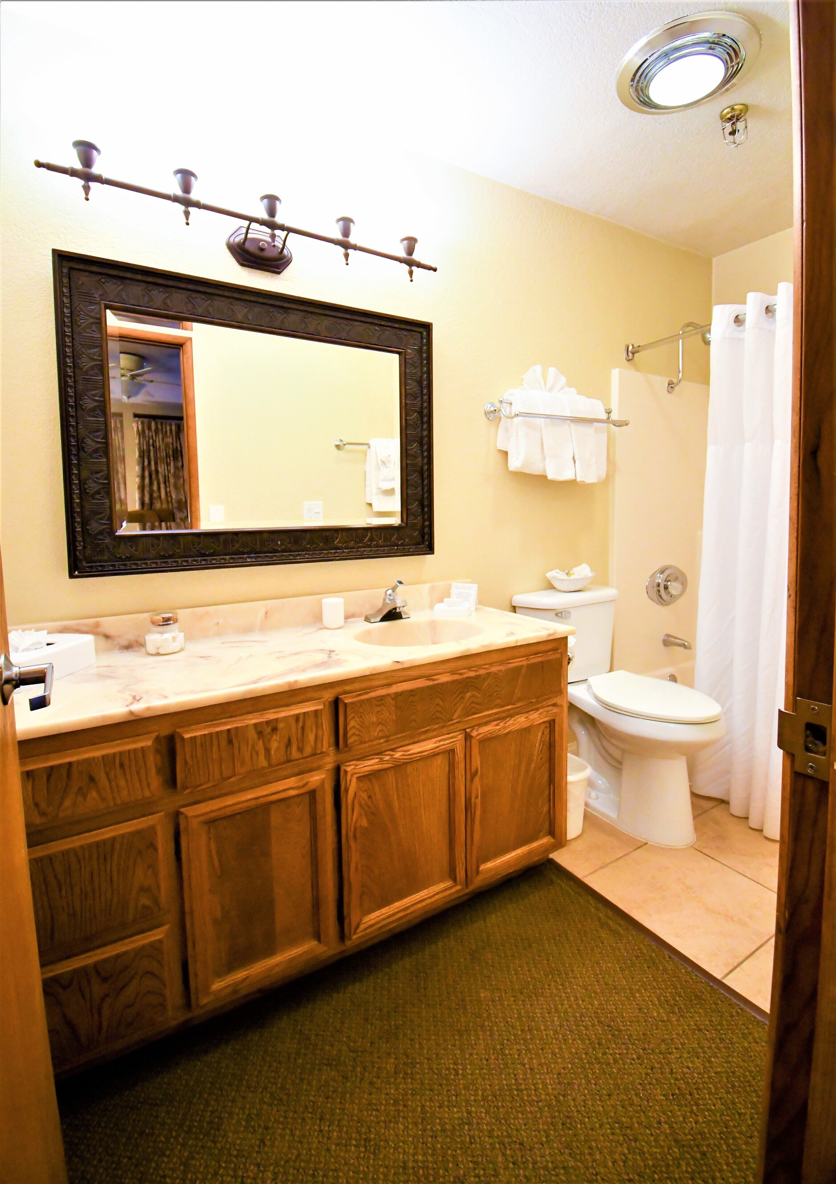 A bathroom with a wooden vanity, a large mirror, a sink, a toilet, and a shower curtain.