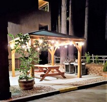A wooden gazebo with string lights, a barbecue grill, and a potted plant.