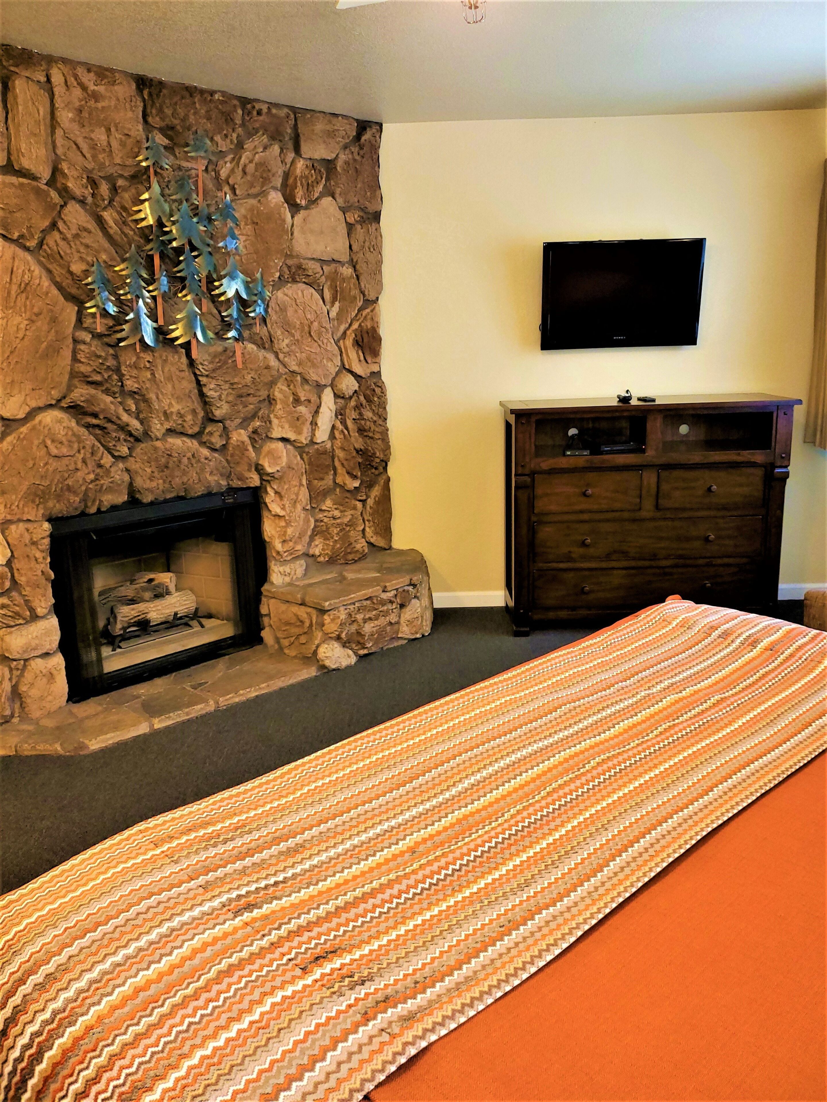 A room with a stone fireplace, a flat-screen TV mounted above it, and a wooden dresser.
