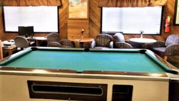 A pool table in a room with wooden walls, two windows, and a ceiling fan.
