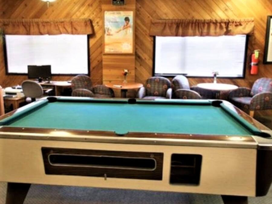 A pool table in a room with wooden walls, two windows, and a ceiling fan.