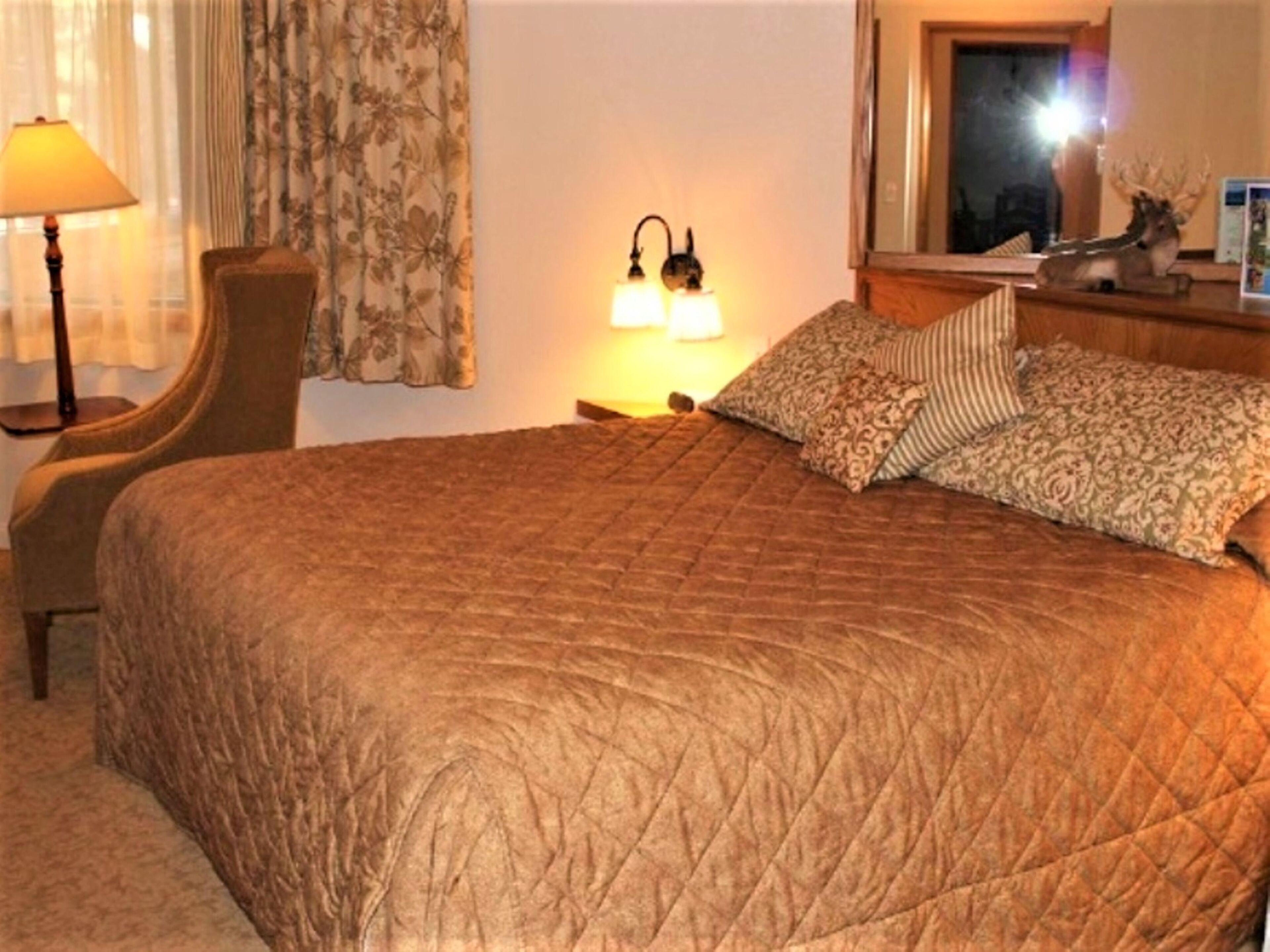 Habitación de hotel con una cama grande, una silla, una lámpara y una mesita de noche con un adorno.