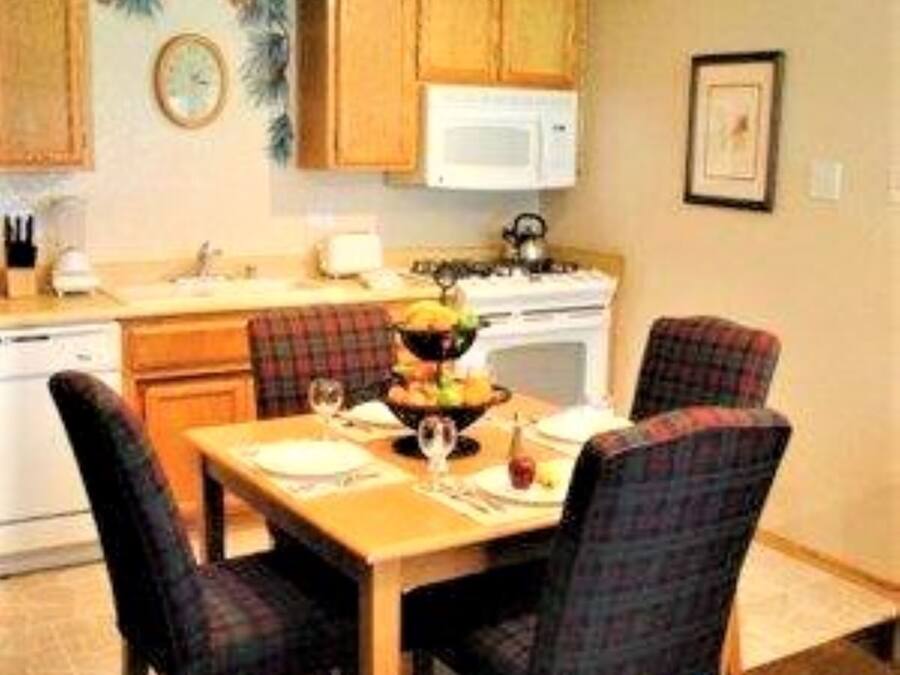 A compact kitchen with wooden cabinets, a microwave, and a dining table with plaid chairs.