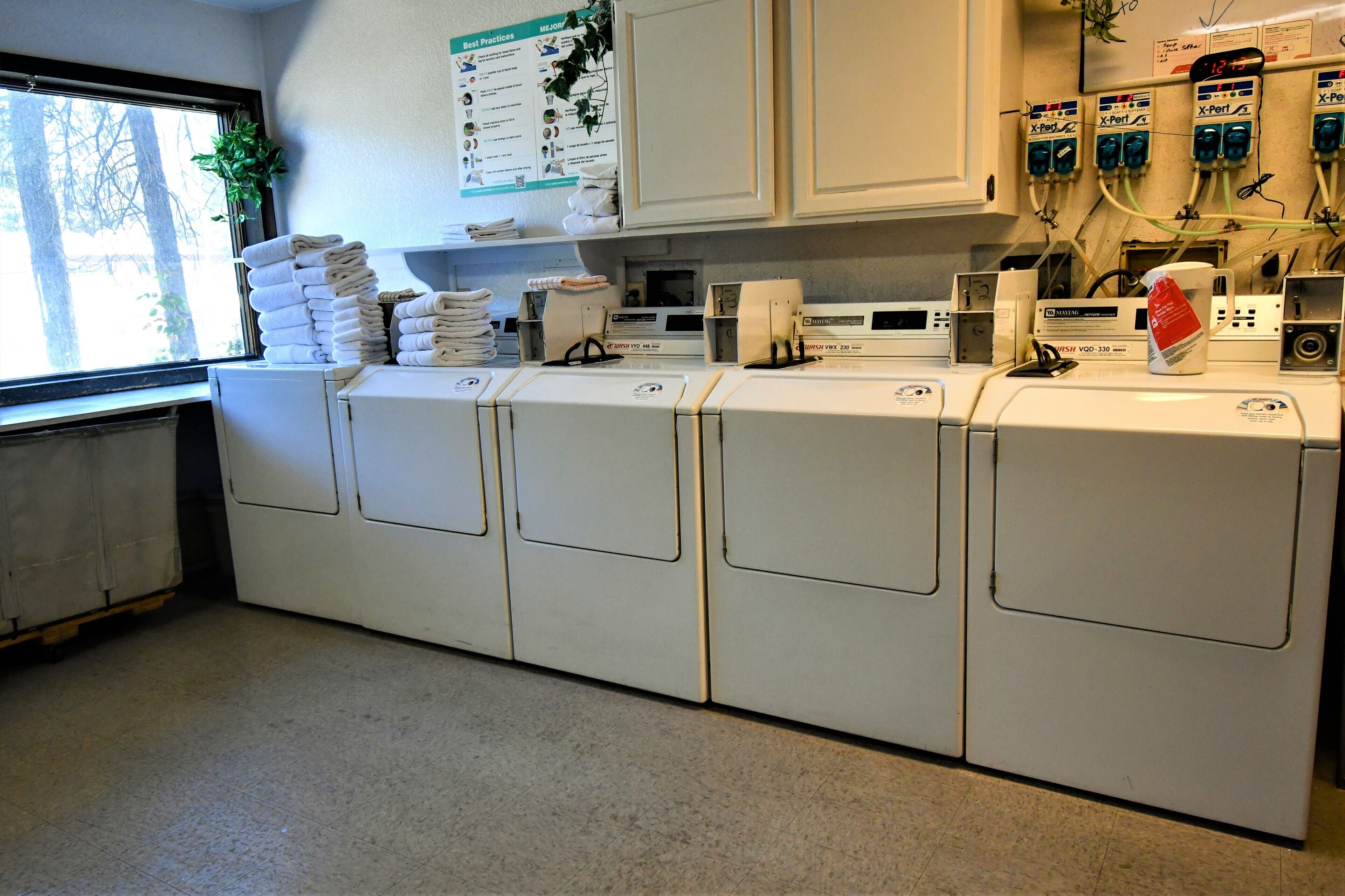 A laundry room with stacked towels, a bulletin board with best practices, and a clock.