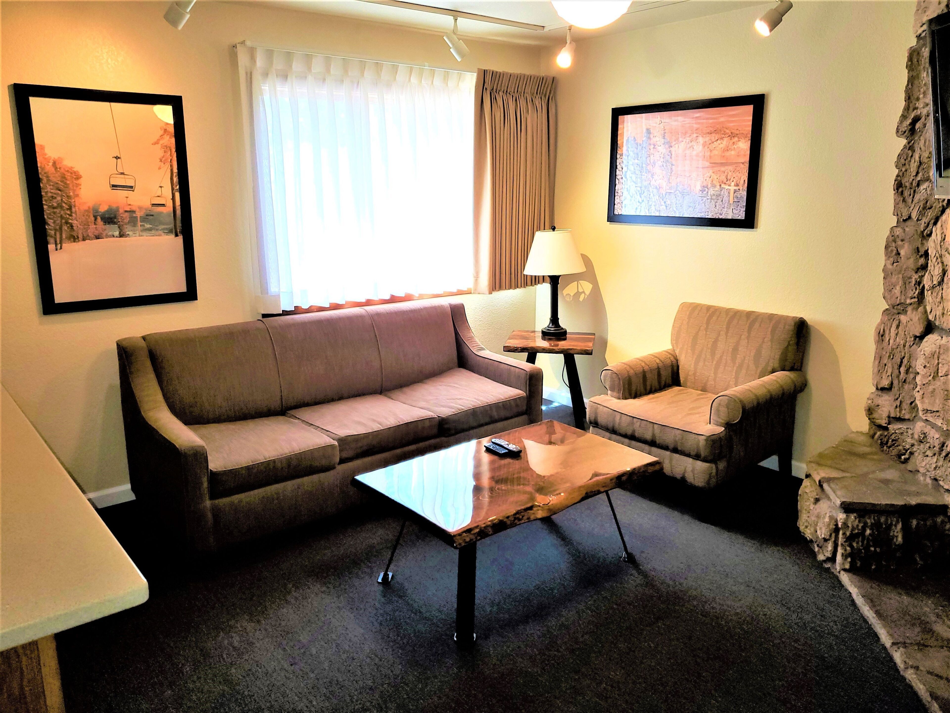 Un salon comprenant un canapé, un fauteuil, une table basse, une lampe et un mur d’accent en pierre.