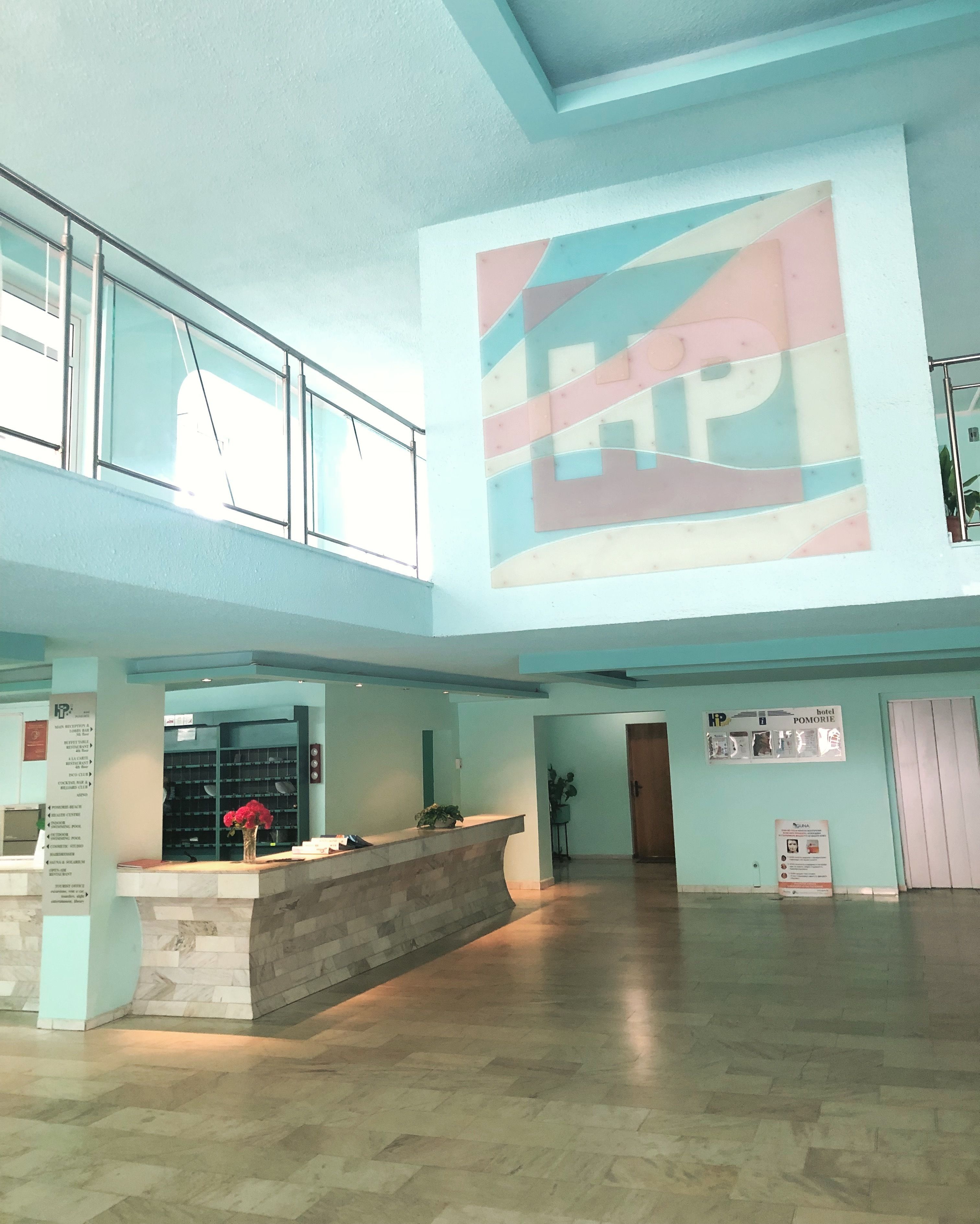 A spacious lobby with a reception desk, a large abstract mural, and a staircase leading to an upper level.