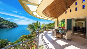 A balcony with a view of the ocean, wicker furniture, and a dining area with a table and chairs. - Luxury Beach Frontage Villa For Rent (Boca de Tomatlán)