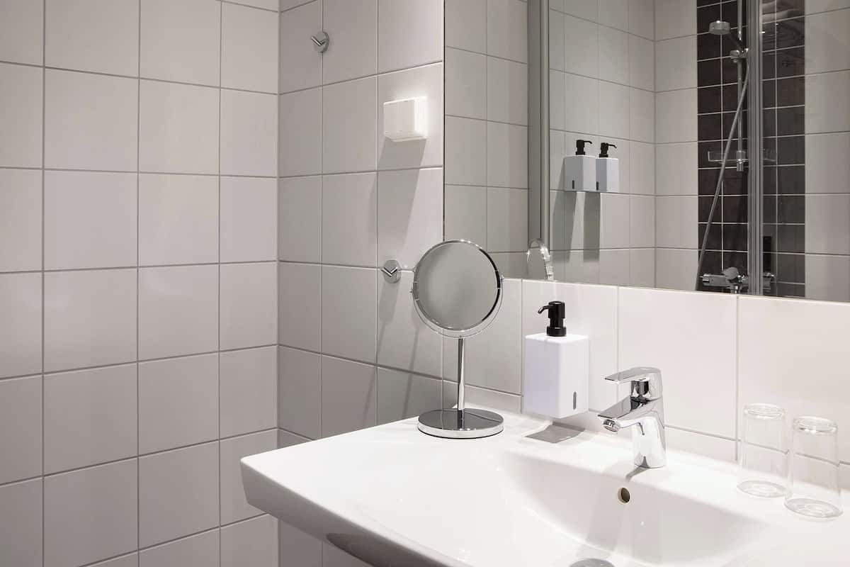 Un baño moderno con azulejos blancos, un espejo redondo, un lavabo y una zona de ducha.