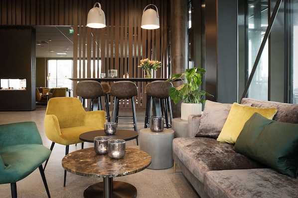 A modern lounge area with a sofa, chairs, a round table, and a bar area.