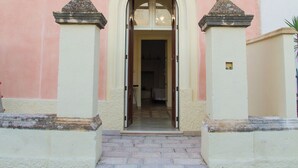 A building entrance with a pink facade, a central doorway, and two small columns on either side. - Le Tenute di Agnese (Alliste)