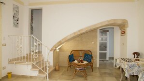 A spacious living area with a staircase, a dining table, and a wicker sofa. - Le Tenute di Agnese (Alliste)