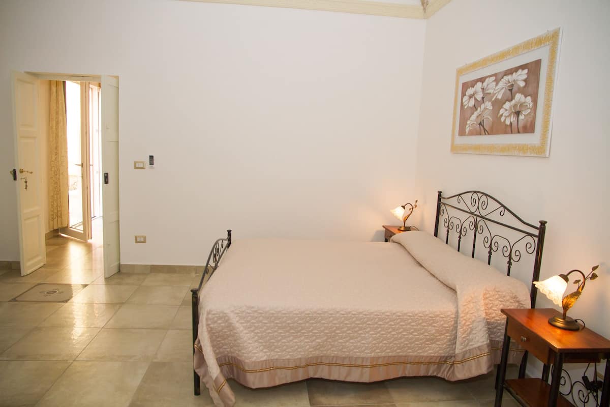 A bedroom with a bed, bedside lamps, a door, and a wall-mounted painting.