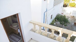 A balcony with a stone balustrade overlooking a courtyard with a small tree and a white wall. - Le Tenute di Agnese (Alliste)