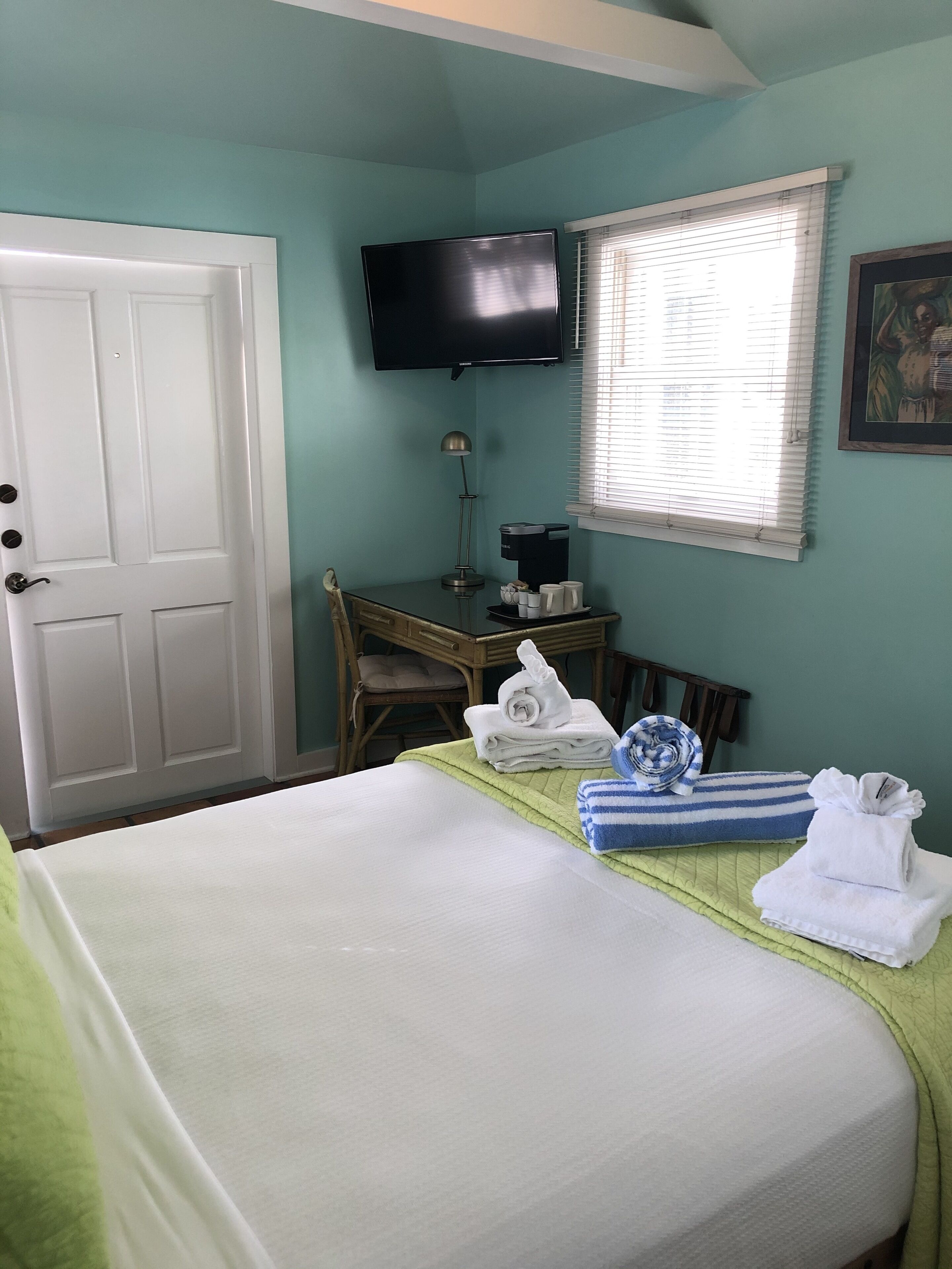 Une chambre d’hôtel équipée d’un lit, d’un bureau, d’une chaise, d’une télévision et d’une fenêtre avec des stores.