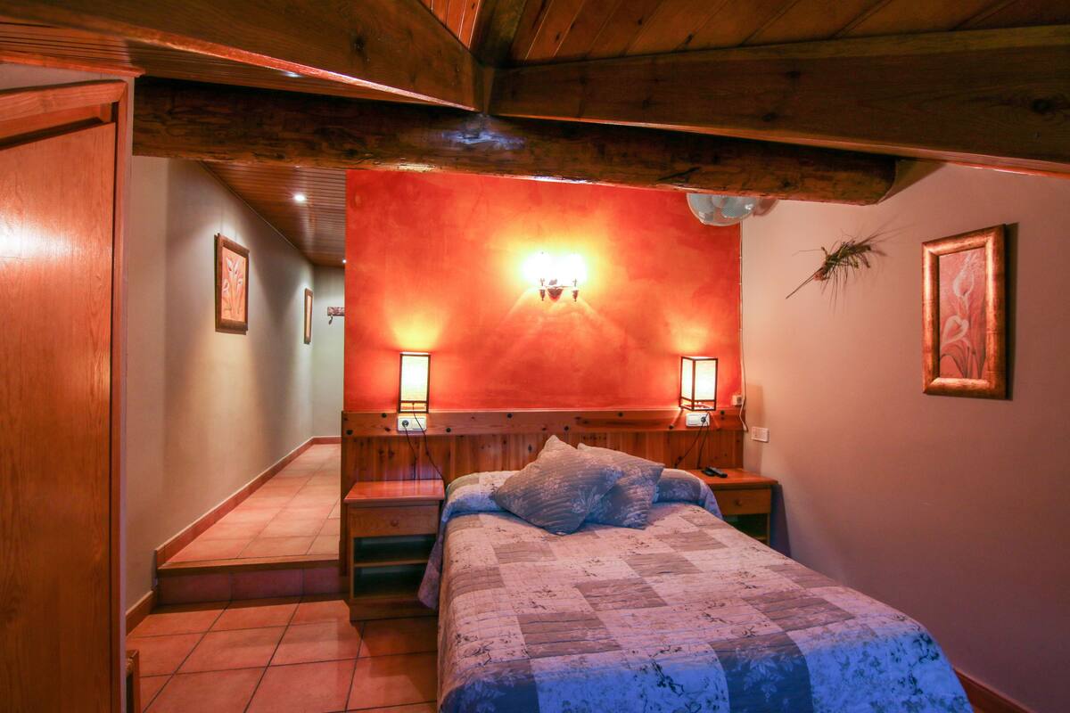 A bedroom with a wooden ceiling, a bed with a quilt, two bedside lamps, and a framed picture on the wall.
