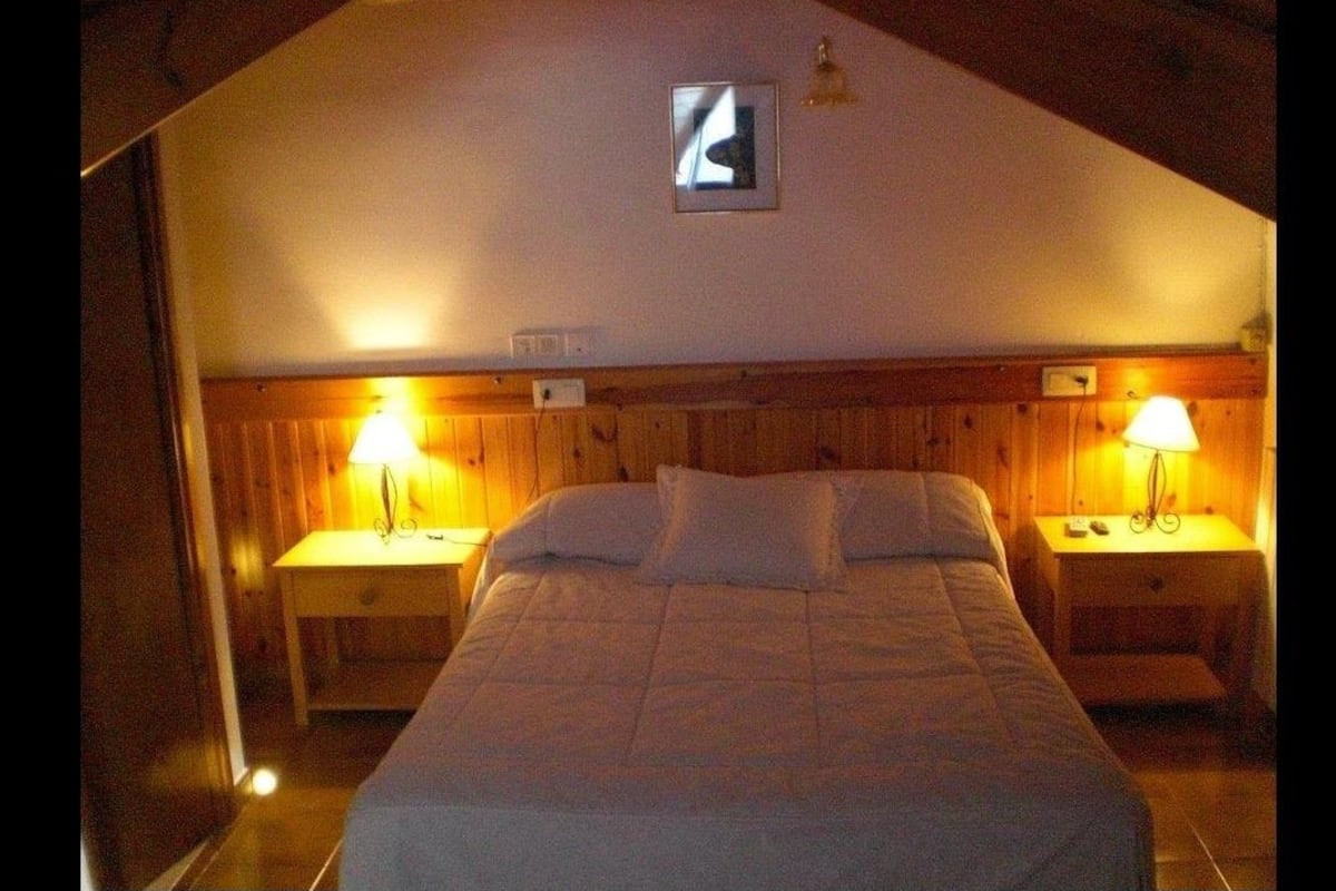 A bedroom with a wooden headboard, two bedside tables with lamps, and a bed with white bedding.