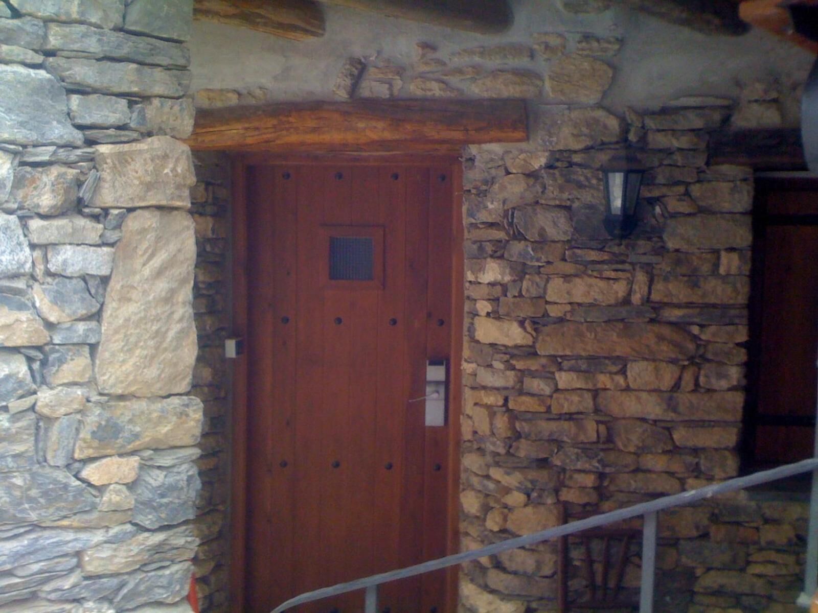 Un mur de pierre avec une porte en bois, une rampe en métal et un escalier en pierre.