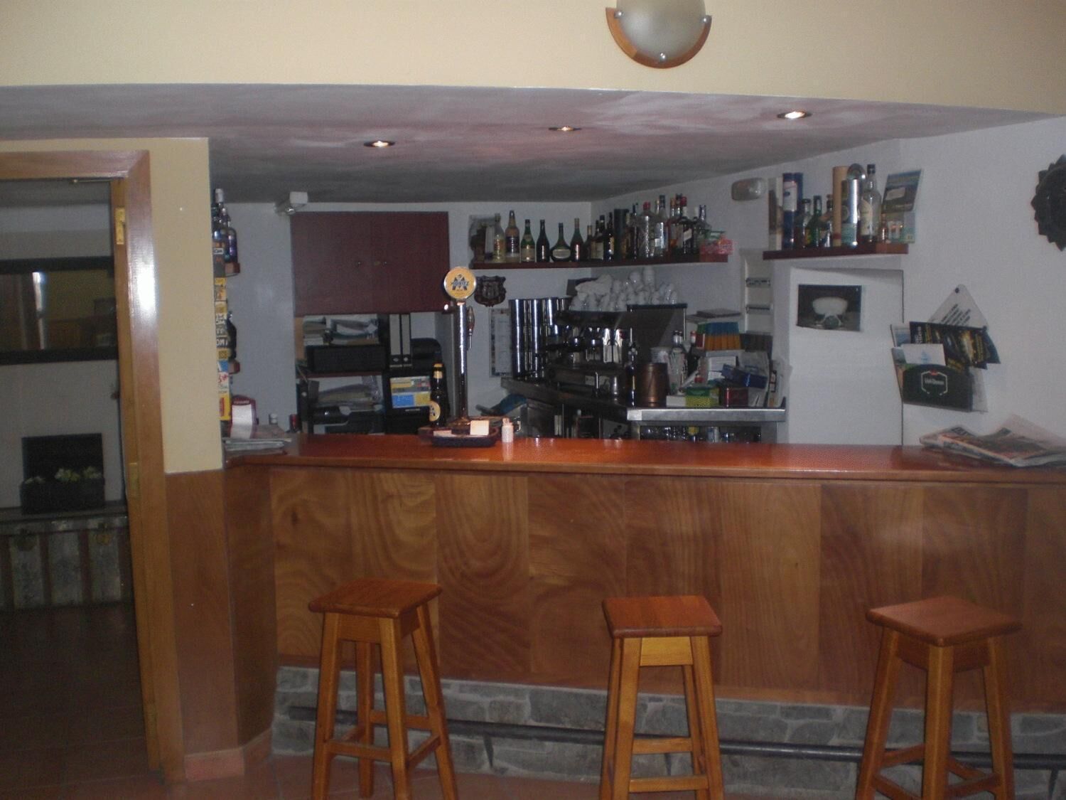 A bar area with wooden stools, a counter, and shelves stocked with bottles.
