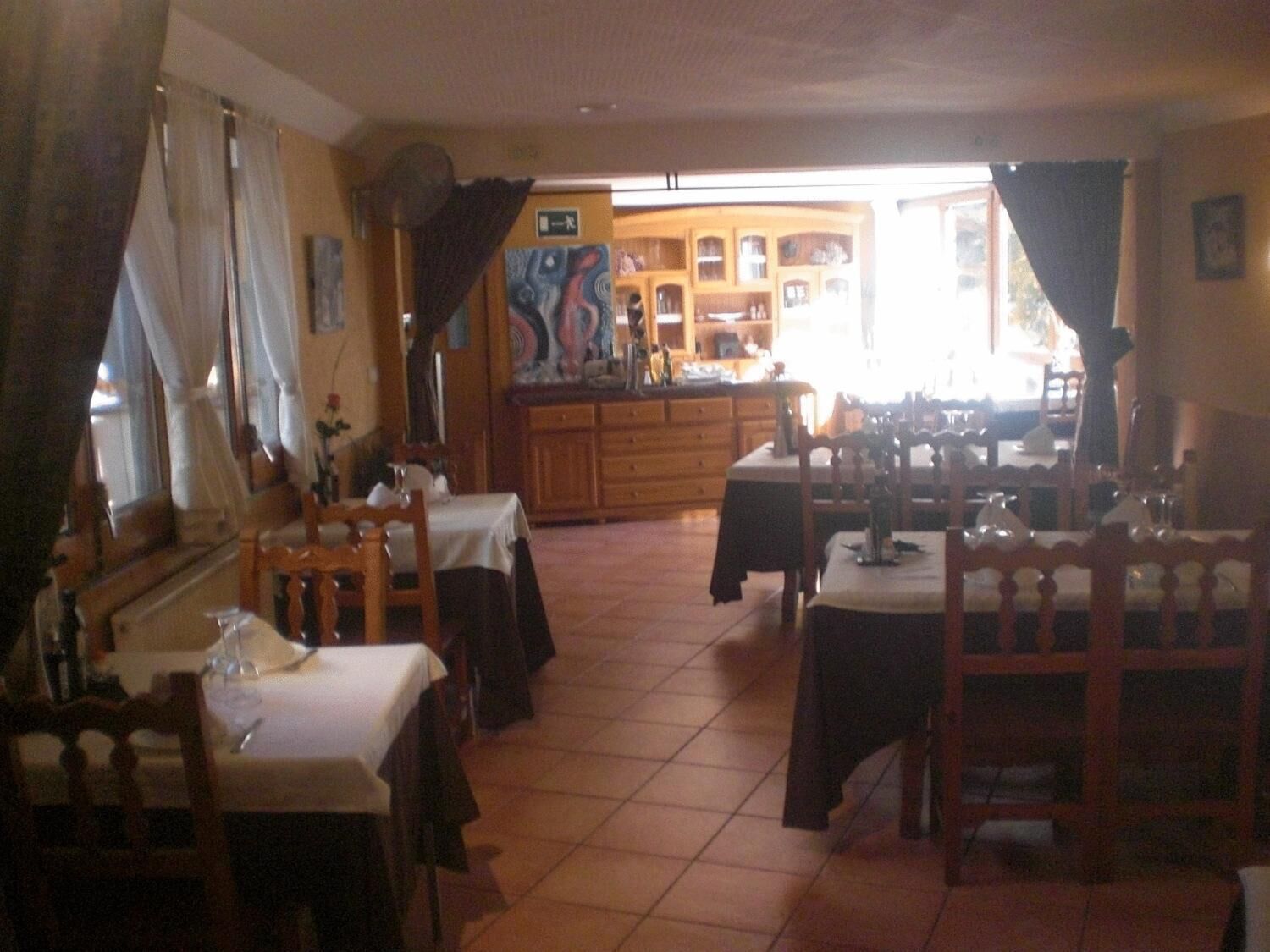 Un ristorante con diversi tavoli e sedie, una zona cucina sullo sfondo e vista sulla strada.