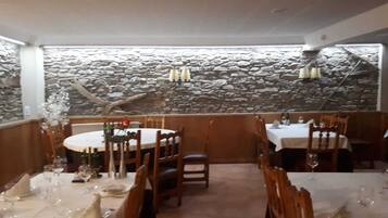 A restaurant with stone walls, round tables, and wooden chairs.