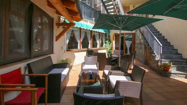 An outdoor patio area with wicker furniture, a table, and a staircase leading to an upper level. - Hotel Roch (Sort)