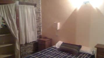 A bedroom with a bed, a nightstand, a lamp, a window with curtains, and a stone wall.