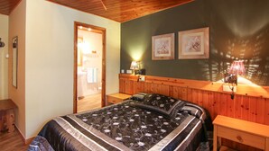 A bedroom with a wooden ceiling, a bed with a floral bedspread, a nightstand, a wall-mounted lamp, and two framed pictures. - Hotel Roch (Sort)