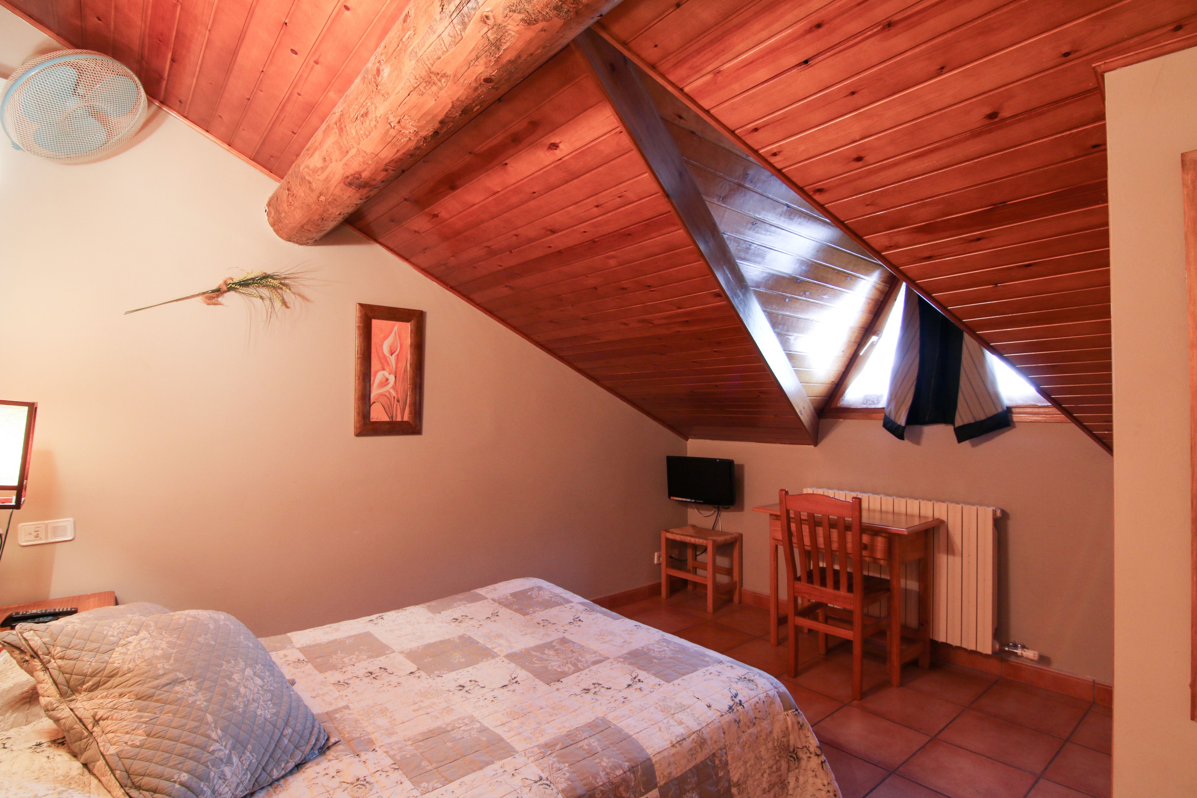 A bedroom with a sloped ceiling, a bed with a quilt, a chair, a small table, a television, and a radiator.