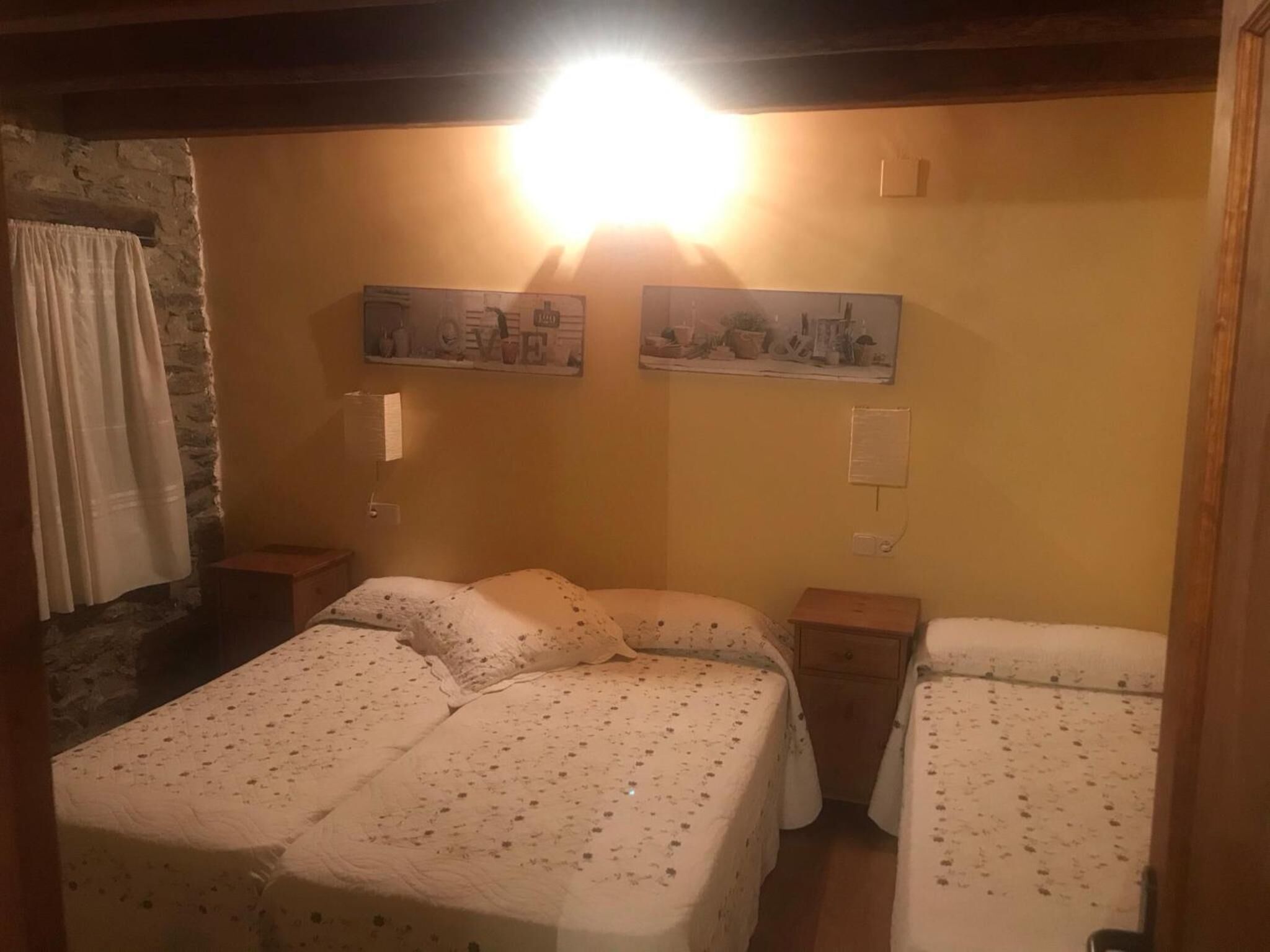 Una stanza con due letti, un muro in pietra e due quadri appesi.