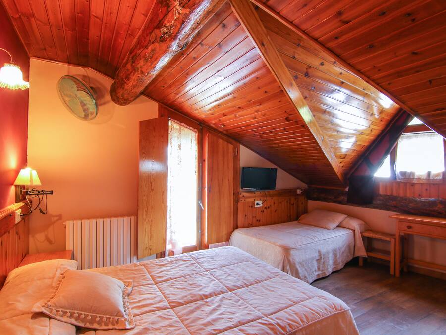 A cozy attic bedroom with two beds, a desk, and a television.