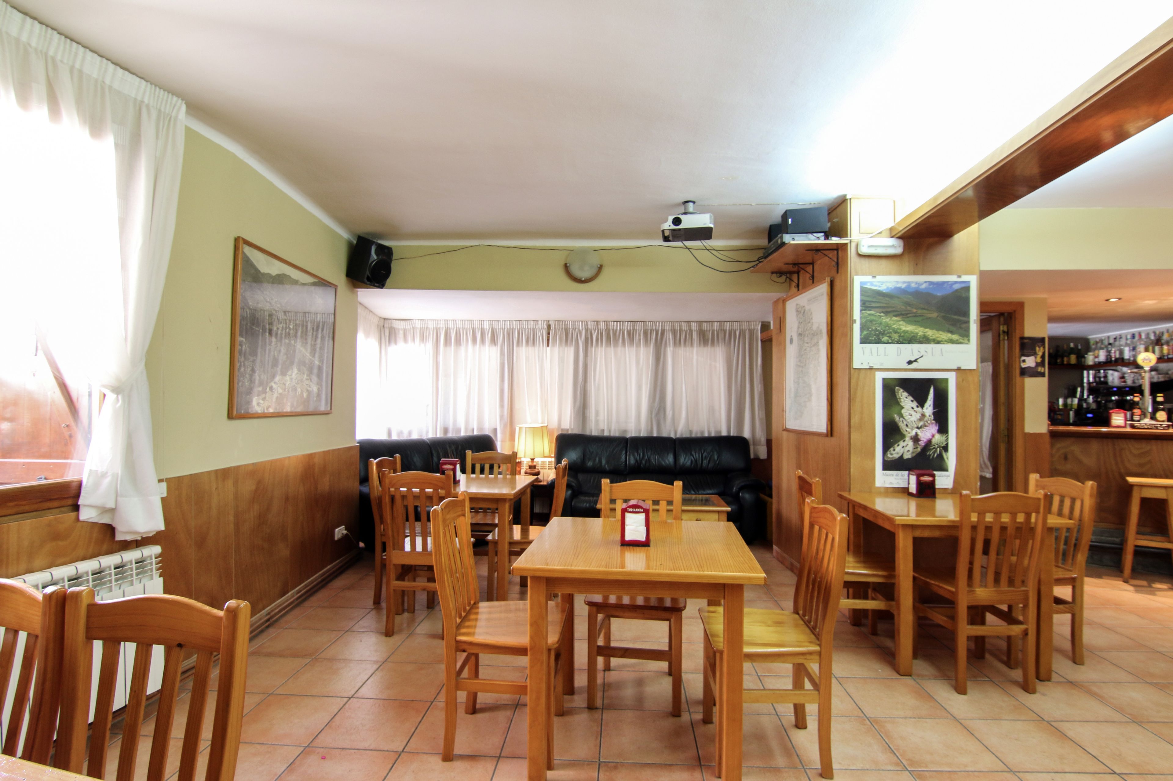 A dining area with wooden tables and chairs, a black leather sofa, and a bar area with bottles.