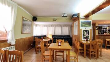 A dining area with wooden tables and chairs, a black leather sofa, and a bar area with bottles.