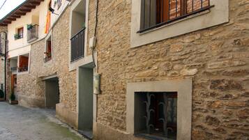 Un edificio de piedra con balcones, una ventana pequeña con celosía metálica e una bandera.
