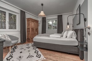 A bedroom with a bed, a chair, a wardrobe, a hanging light fixture, and a window.