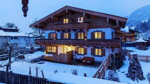 Un chalet en bois à deux étages, doté d’un balcon, d’une terrasse en bois et surplombant un paysage enneigé.