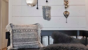 Une pièce comprenant un banc noir, un pouf moelleux, un tapis à motifs, un miroir fixé au mur et des objets décoratifs.