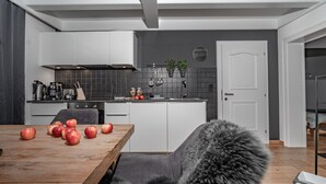 Une cuisine moderne avec des meubles blancs, une table en bois sur laquelle sont posées des pommes et une chaise grise.