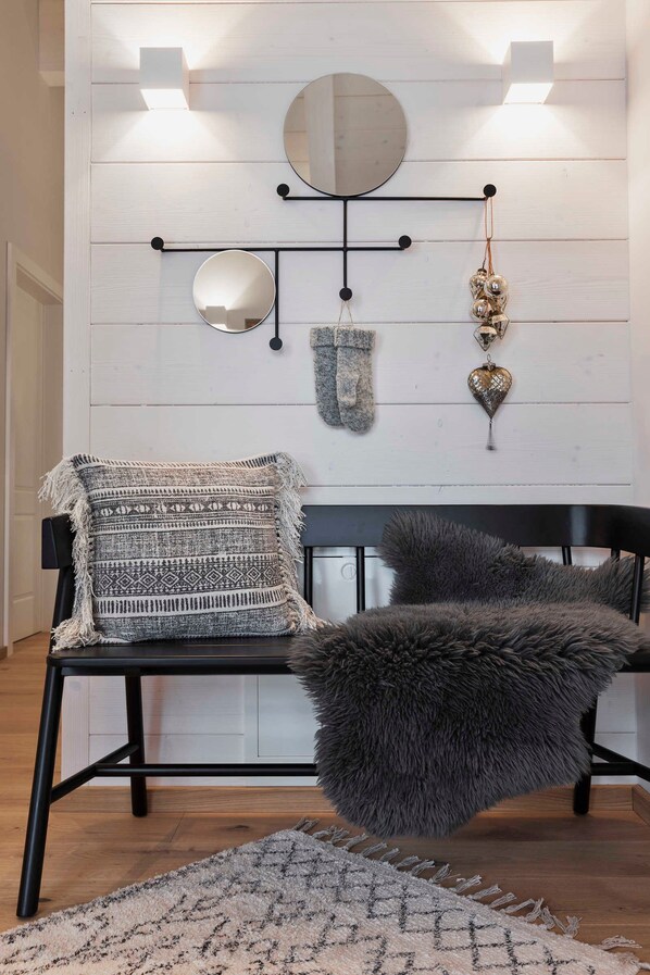 Una habitación con un banco negro, un reposapiés mullido, un tapete estampado, un espejo adosado a la pared y objetos decorativos.