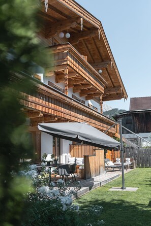 A wooden chalet with a balcony, outdoor seating, and a view of the mountains.