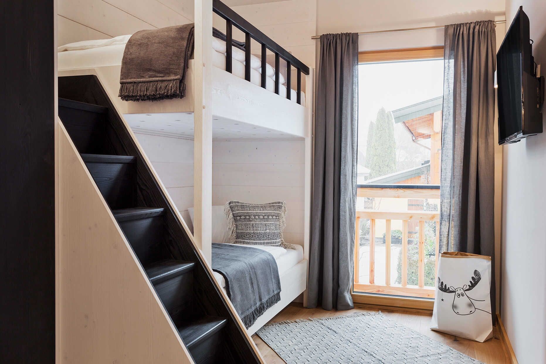 Ein Zimmer mit Etagenbett, einer Treppe, einem Vorhangfenster und einer Tasche mit Elchmuster.