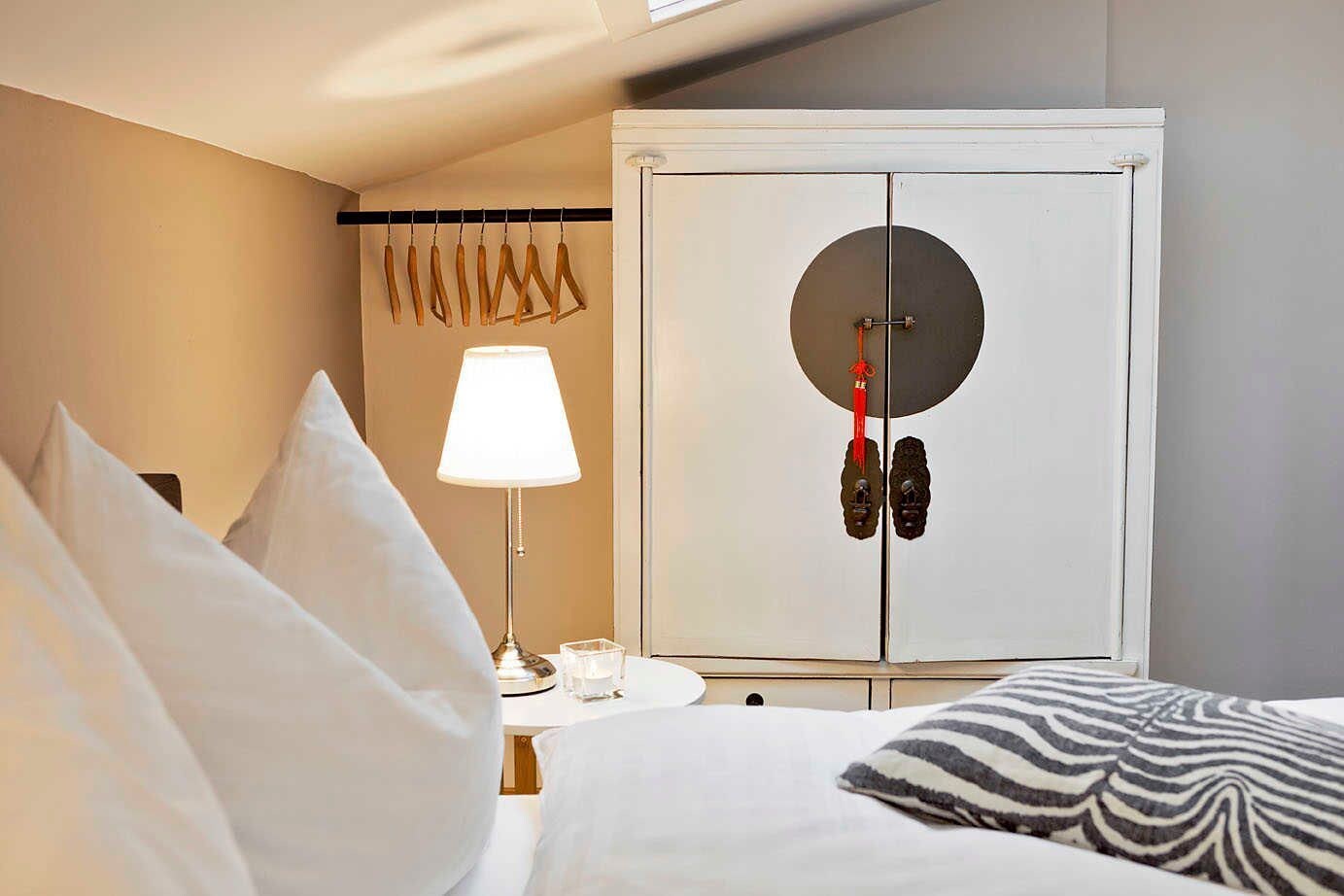 A hotel room with a bed, a nightstand with a lamp, a wardrobe, and a window.